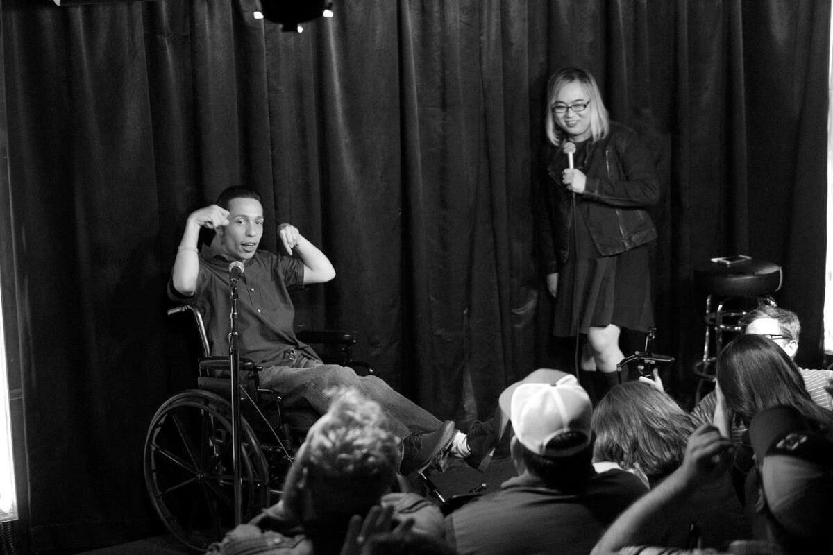 A man in a wheelchair and a woman with a microphone perform in front of a crowd.