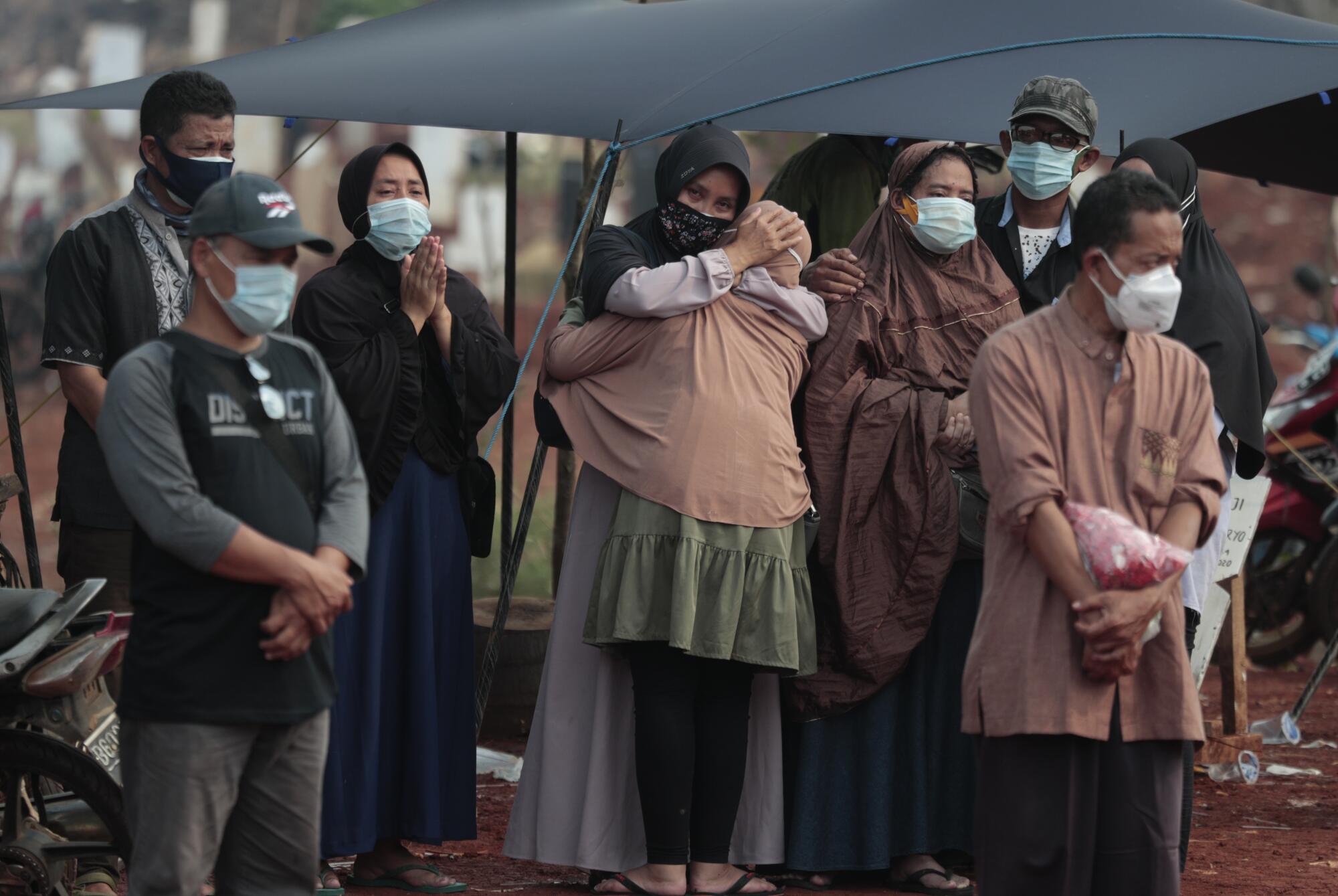 People wearing face masks attend a burial.