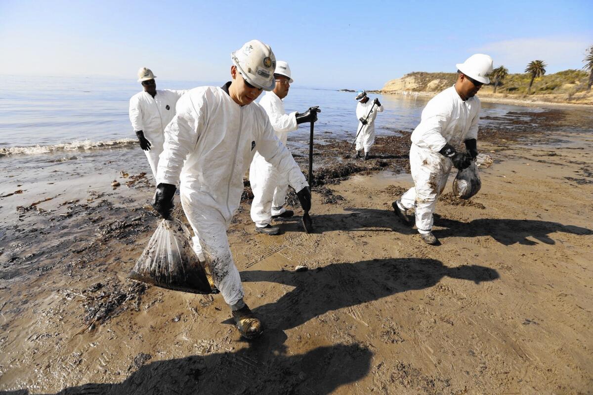 Workers in white uniforms carry oil-fouled sand from a beach
