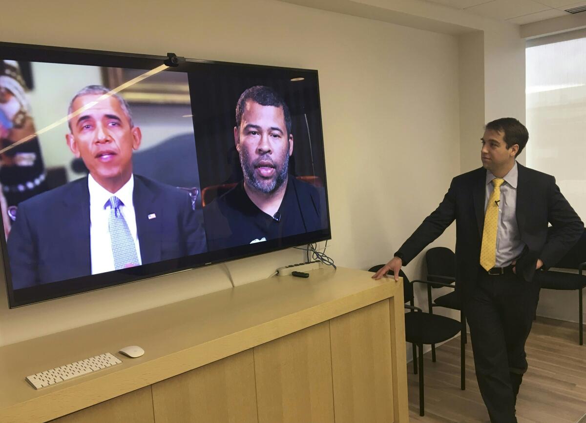 A man stands next to a split screen showing a deepfake video of one man, left, saying words uttered by another, right.
