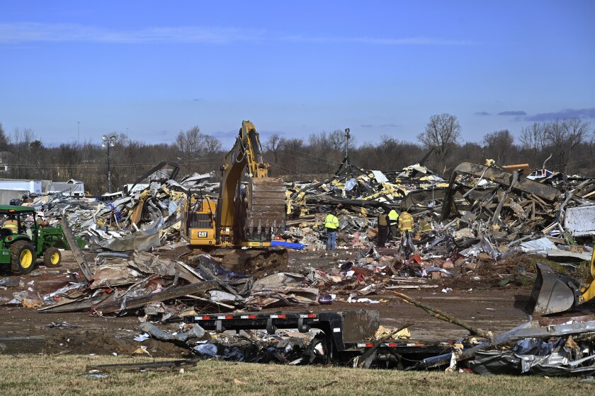 Search crews use heavy machinery to dig through the rubble of a candle factory in Mayfield, Ky.