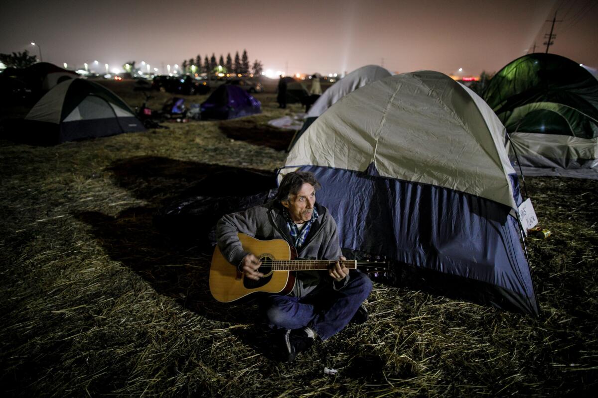 Chris Yarbrough, who lost his home in the Camp fire, plays a donated guitar in a tent city set up by evacuees in a Chico parking lot. (Marcus Yam / Los Angeles Times)