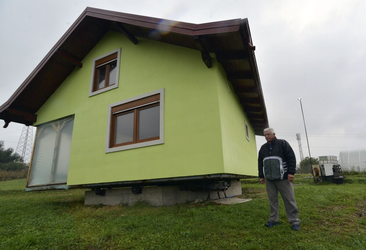 Vojin Kusic's stands in front of his rotating house in a town of Srbac, northern Bosnia, Sunday, Oct. 10, 2021. The house designed and built by 72-year-old Vojin Kusic, with its green façade and red metal roof, can rotate a full circle to satisfy his wife's shifting desires as to what she should see when she looks out of the windows of her home. (AP Photo/Radivoje Pavicic)