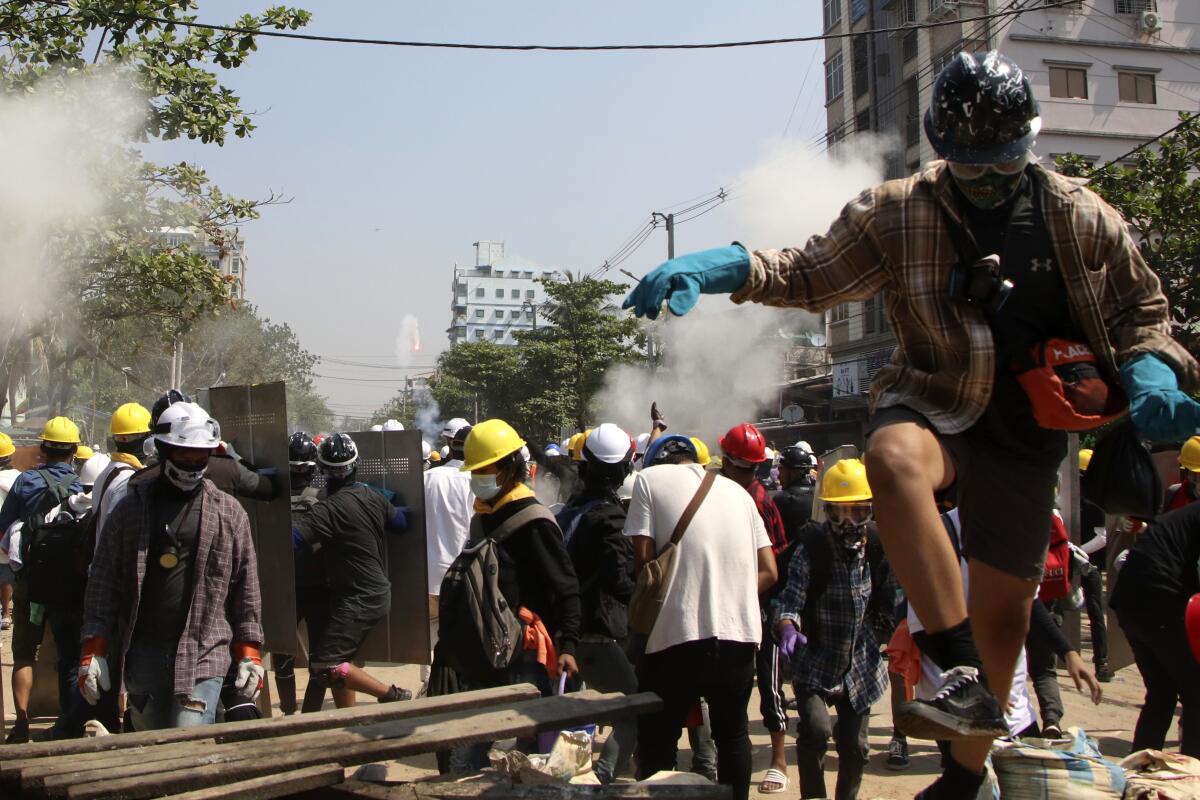 People in hard hats and masks gather in a street; some hold up metal shields.