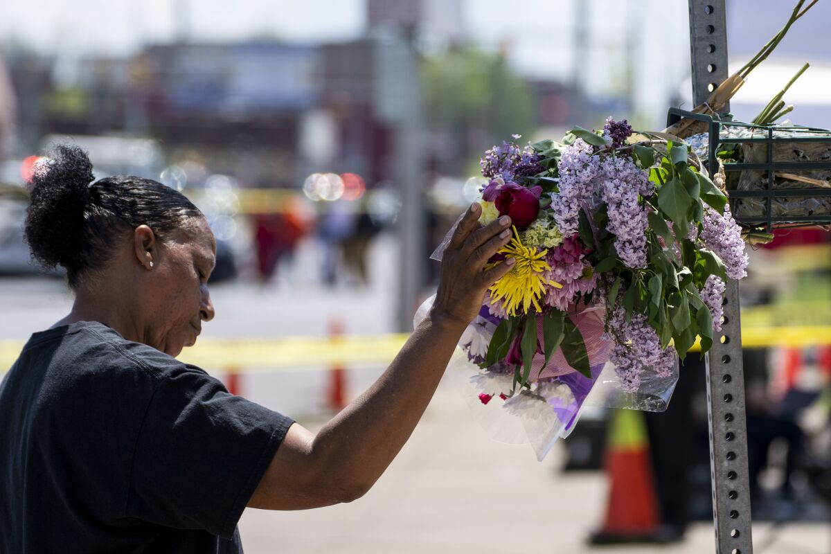 A woman pauses with her hand rested on bunches of flowers tied to a pole