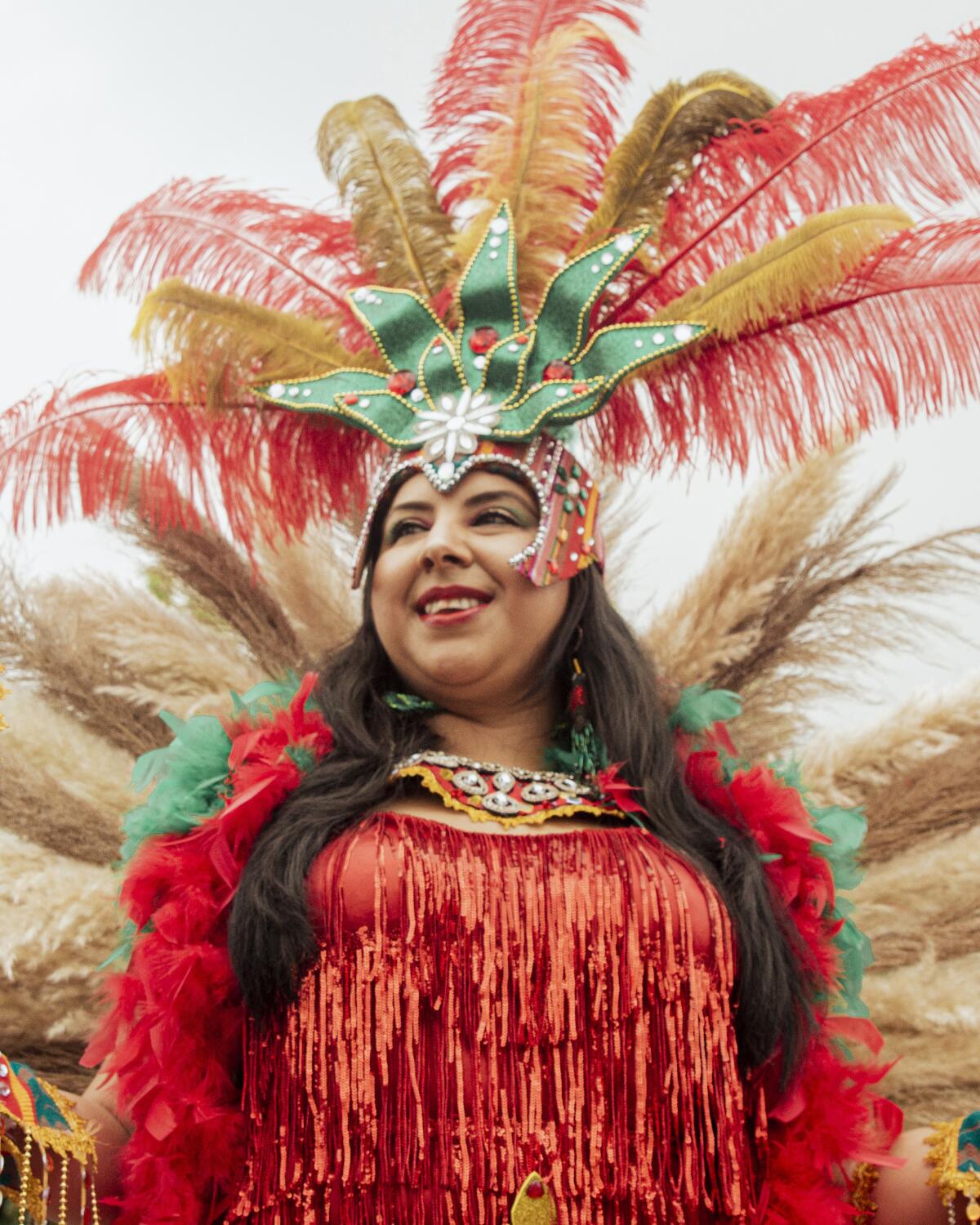 A woman wears a green headdress with red plumes and a red top.