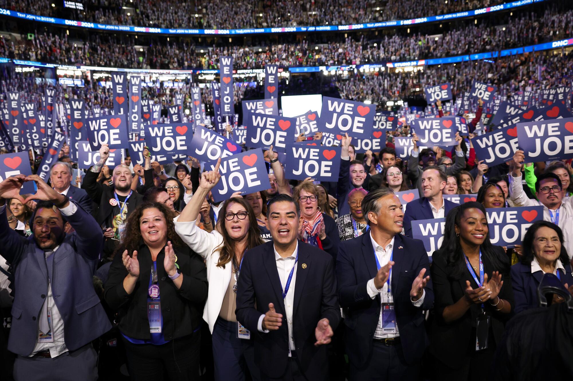     Reps. Robert García, centro, aplaude mientras el presidente Biden habla el lunes con los delegados de California.