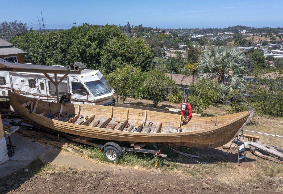 Two men build a boat in a yard.