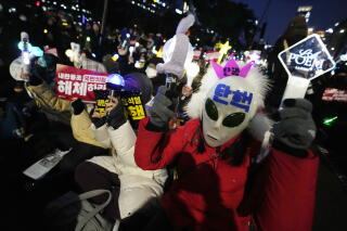 A huge crowd, holding flags, throng the street near buildings