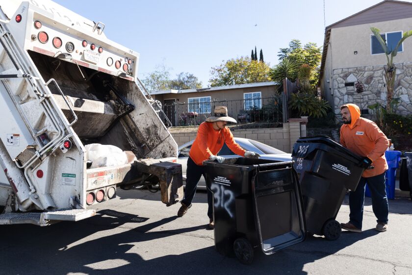Refuse packers Andrew Ruvalcaba and Julian Trujillo load waste onto a garbage truck in Encanto on Friday, Nov. 25, 2022. Neighborhoods like Encanto have “hard-to-collect” streets, requiring rear loader trucks that are easier to navigate in tight spaces.