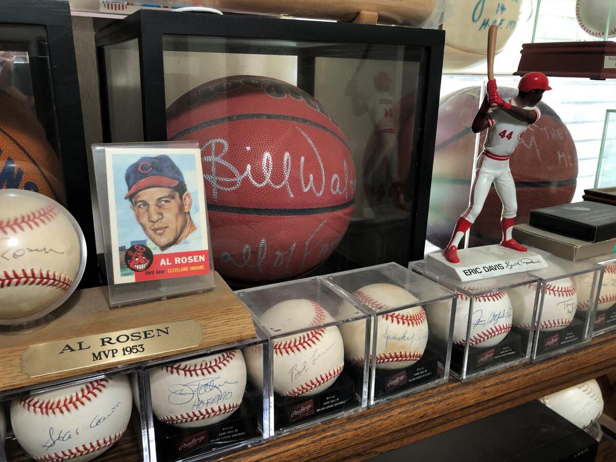 An Al Rosen baseball card and Eric Davis figure sit atop a row of autographed baseball's at Rick Obrand's home.