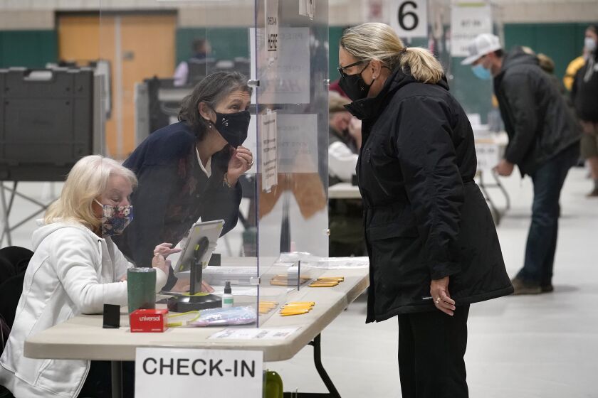 FILE - A poll worker, center left, speaks through a plastic barrier while assisting a voter in a polling station at Marshfield High School, Nov. 3, 2020, in Marshfield, Mass. A bipartisan effort among states to combat voter fraud has found itself in the crosshairs of conspiracy theories fueled by Donald Trump’s false claims about the 2020 presidential election and now faces an uncertain future. (AP Photo/Steven Senne, File)