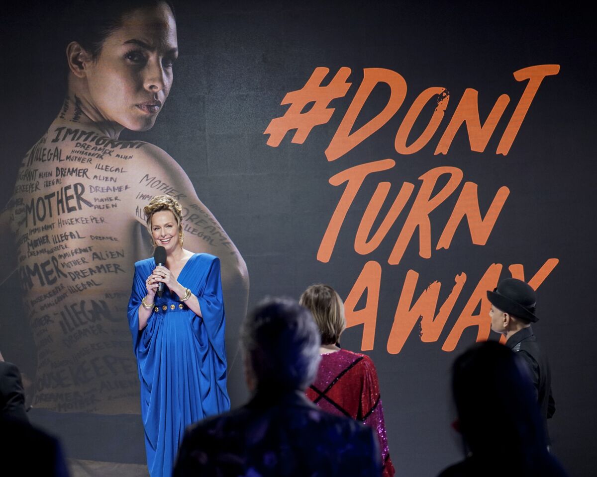 A woman in a blue evening gown standing in front of a mural that says #DontTurnAway