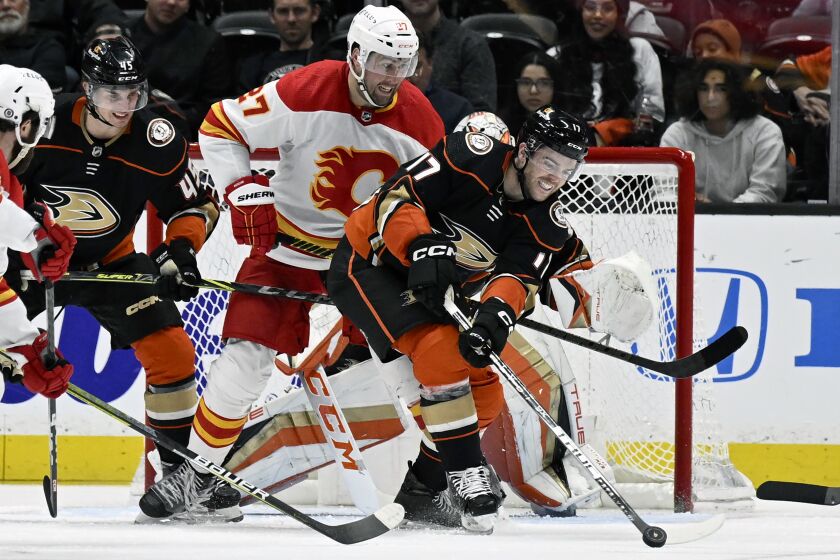 Anaheim Ducks defenseman Scott Harrington, right, clears the puck away from Calgary Flames left wing Nick Ritchie, center, with Ducks defenseman Colton White, left, watching during the third period of an NHL hockey game in Anaheim, Calif., Tuesday, March 21, 2023. (AP Photo/Alex Gallardo)