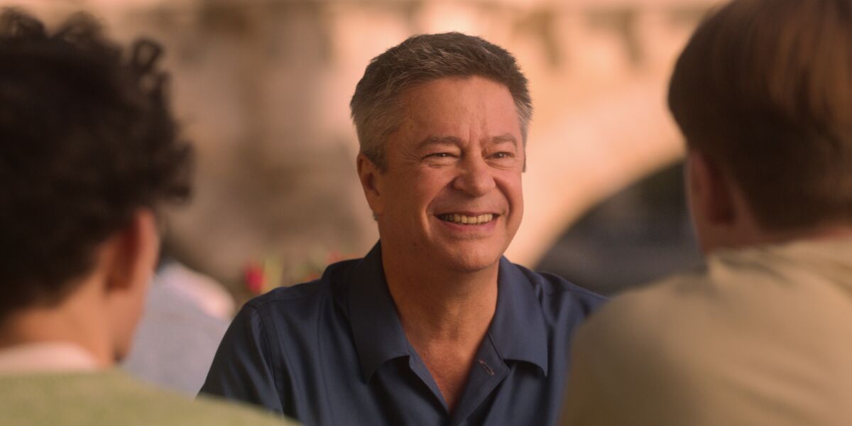 A middle-aged man smiles at two young men facing him