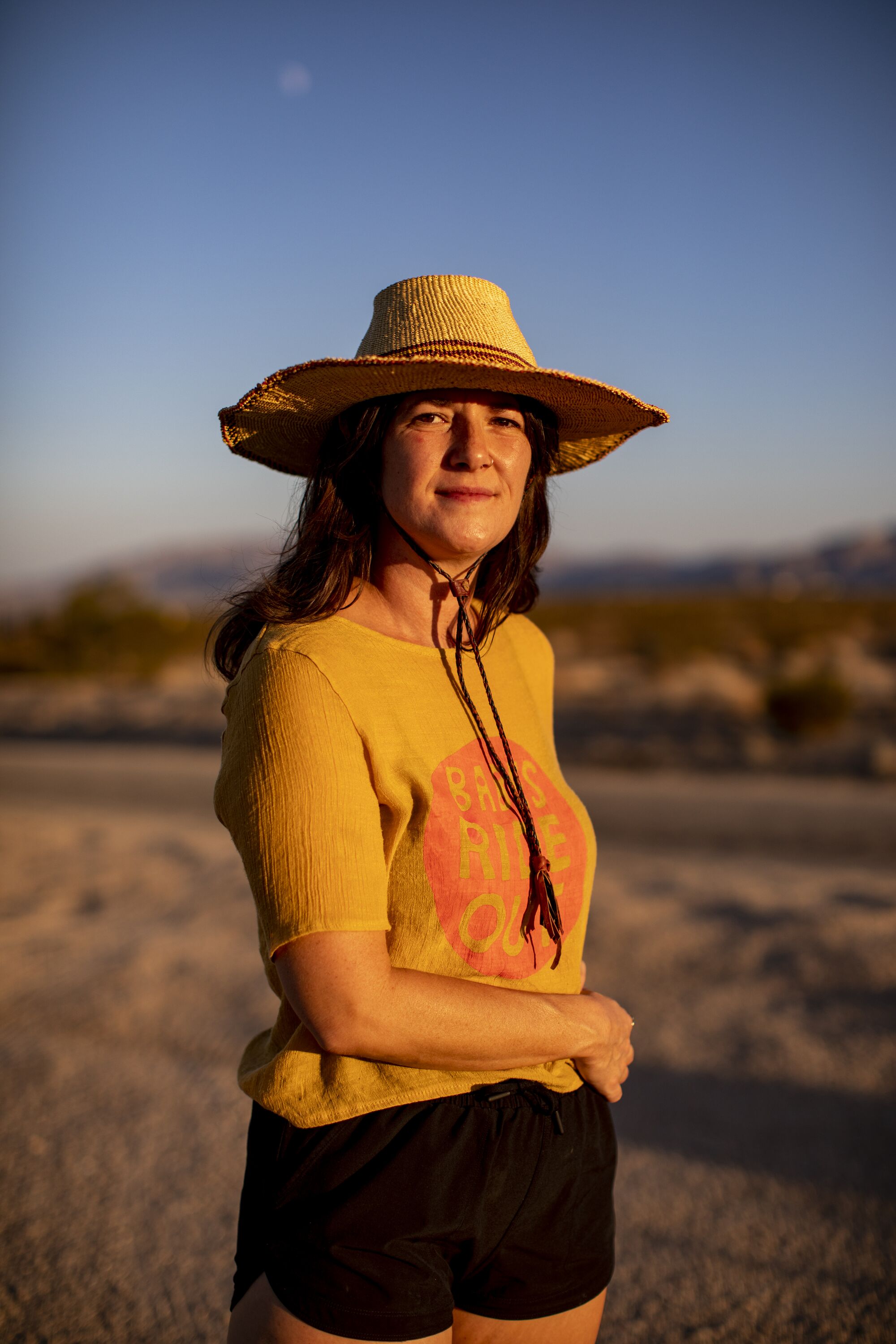 Author Claire Vaye Walkins wears a straw hat, yellow T-shirt and black shorts in the desert.