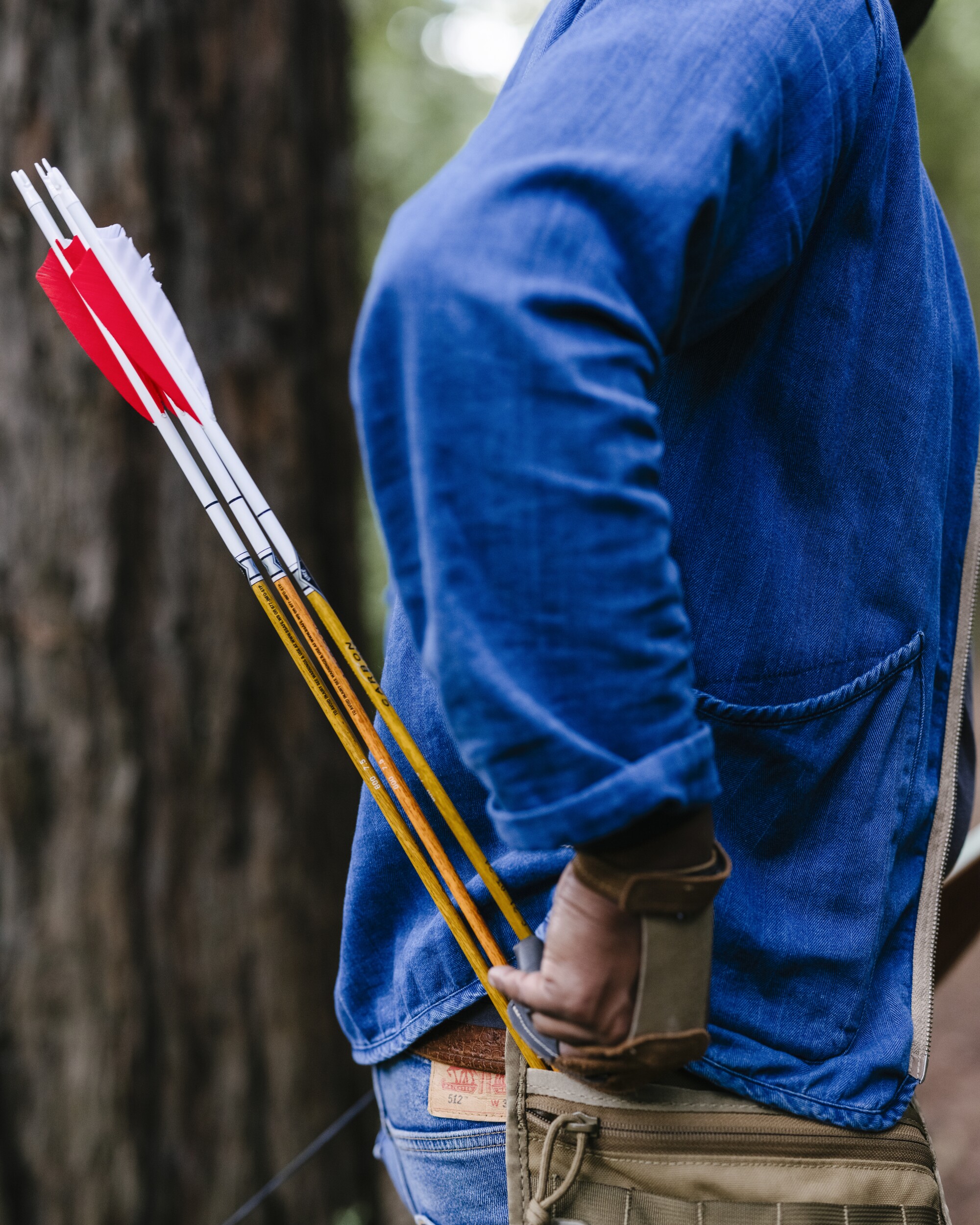 A man in a blue shirt reaches for a quiver of arrows.