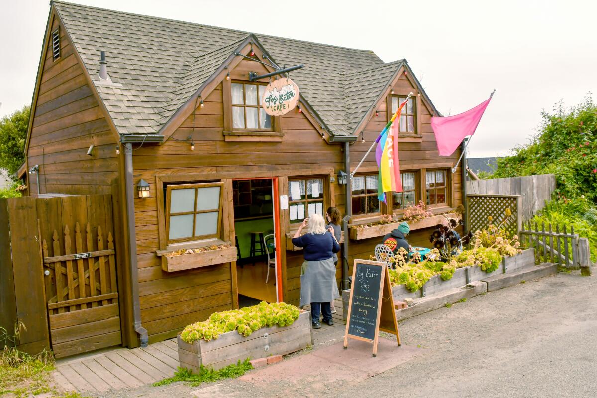 A woman stands outside Fog Eater Cafe, a rustic-looking wooden building.
