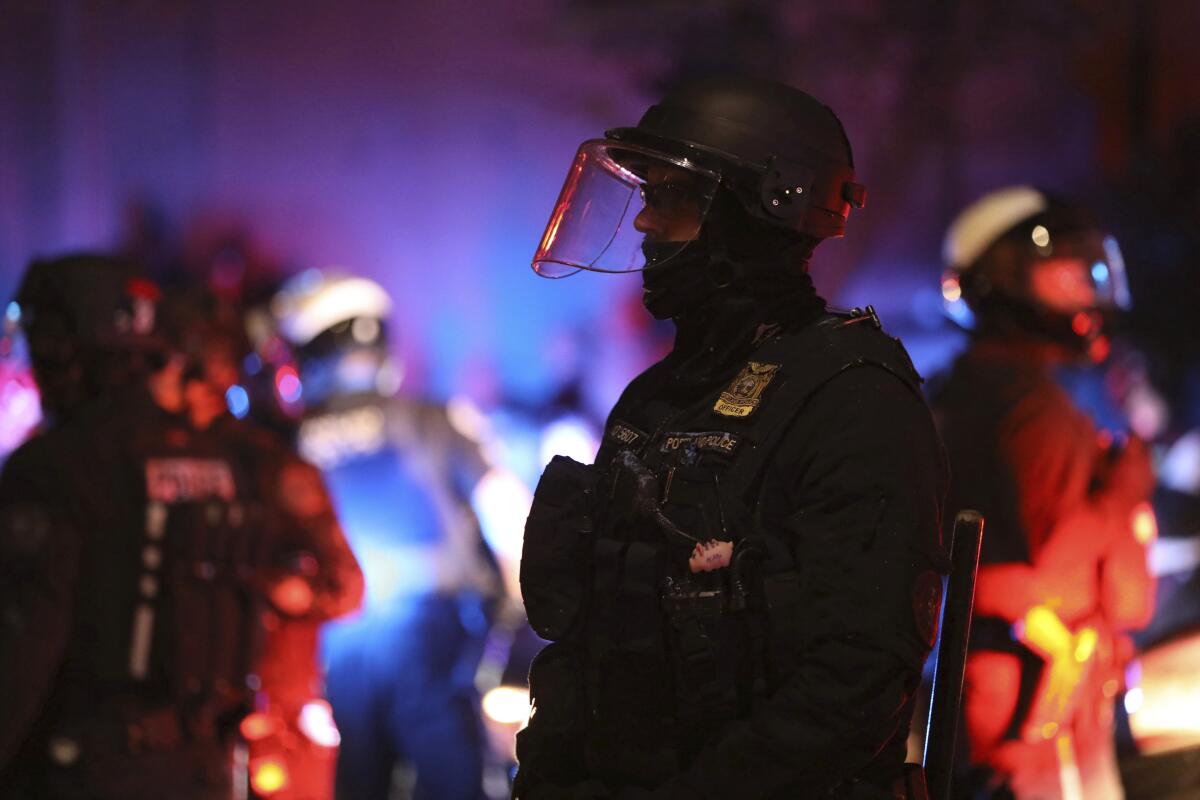 A police officer watches protesters rallying in Portland, Ore.