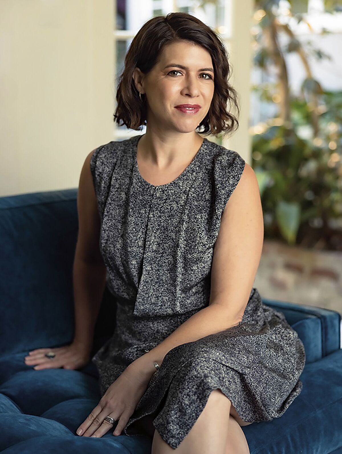 A woman in a dress poses on a couch for a headshot 