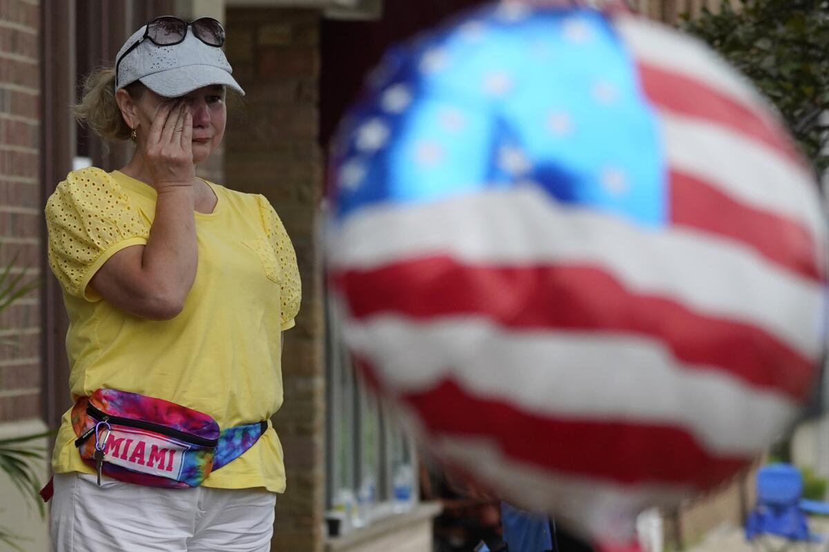 A woman standing behind a red, white and blue balloon wipes away tears