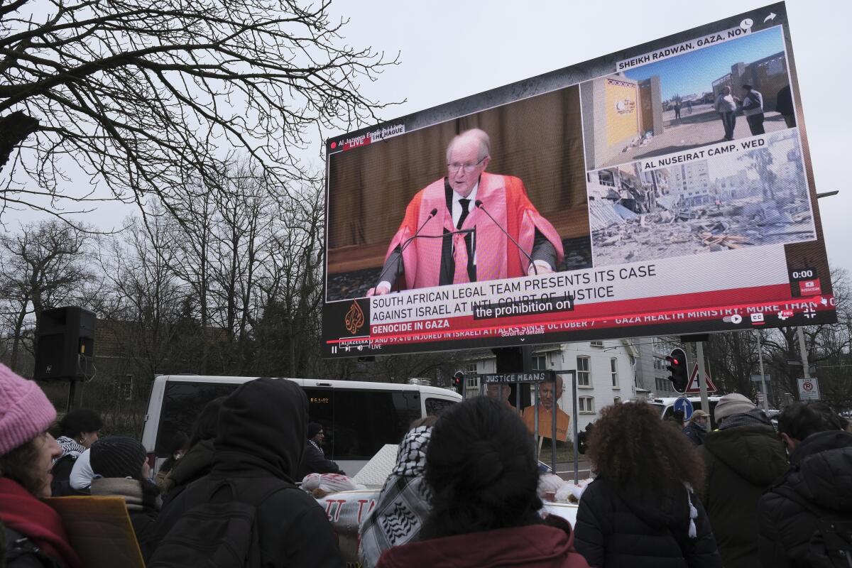 Protesters watch South African legal advisor John Dugard on a large video screen outside the International Court of Justice.