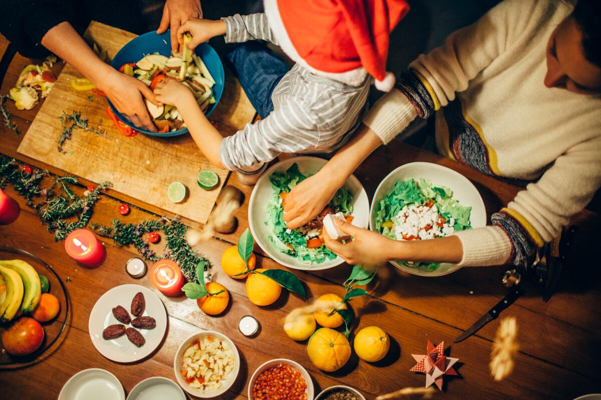 Two adults and a child work on holiday dishes spread across a table. 