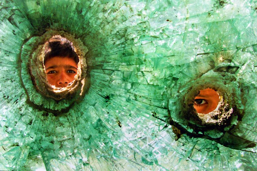 KABUL, AFGHANISTAN-November 19, 2001-At the former Russian embassy abandoned after their defeat, thousands of refugees live in squalid conditions. Two boys peek through bullet holes in the guard station window on November 19, 2001. (Carolyn Cole / Los Angeles Times)