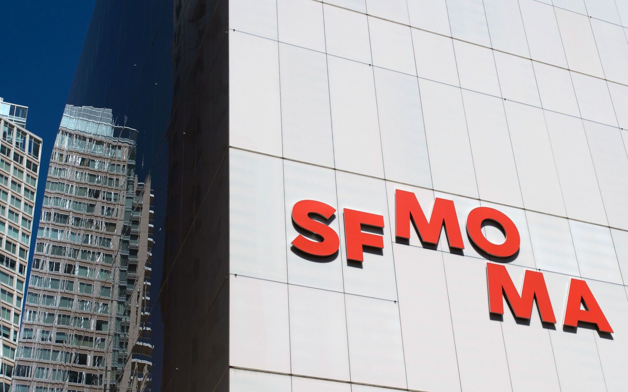 A view of SFMOMA's white facade, bearing the museum's logo in red letters