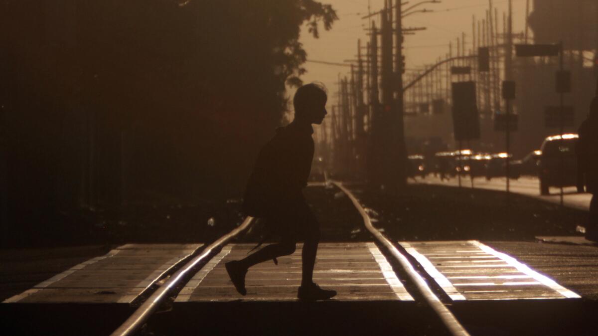A boy walks to school across the railroad tracks at Broadway and Slauson as the early-morning sun drenches the roadway at the beginning of a scorching day on Sept. 15, 2014.