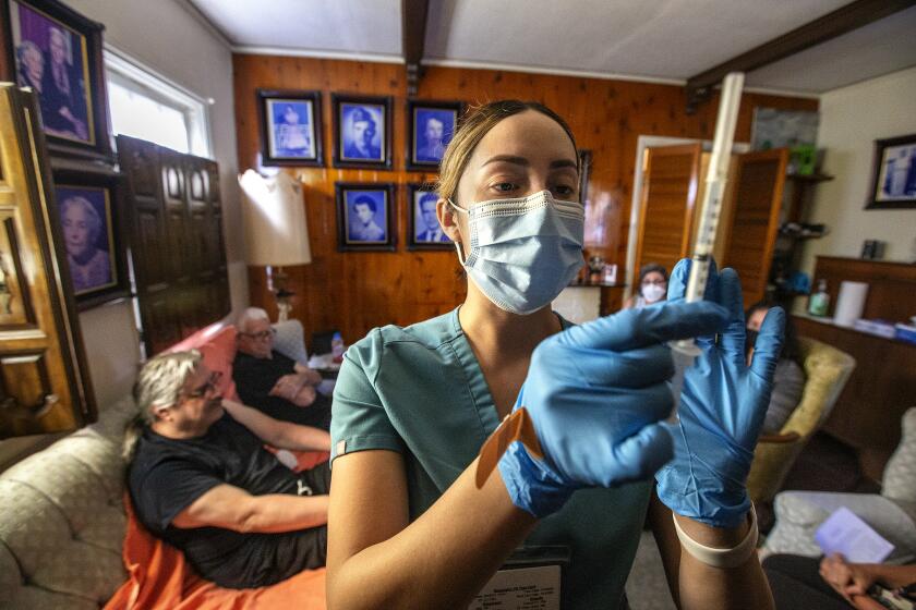 LOS ANGELES, CA-OCTOBER 7, 2022: Licensed Vocational Nurse Angela Tapia prepares a dose of the Moderna COVID-19 booster vaccine at the home of Louis Salazar Jr., 64, foreground, left, and his father Louis Salazar Sr., 90. They both received the vaccine, along with their mother/wife, Maria Salazar, 88. The Los Angeles County Department of Public Health runs a program that provide COVID vaccines to people who are homebound. (Mel Melcon / Los Angeles Times)