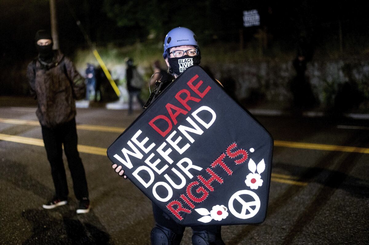 Stacy Kendra Williams holds a shield while facing off against police at the Penumbra Kelly Building on Thursday, Sept. 3, 2020, in Portland, Ore. This weekend Portland will mark 100 consecutive days of protests over the May 25 police killing of George Floyd. (AP Photo/Noah Berger)