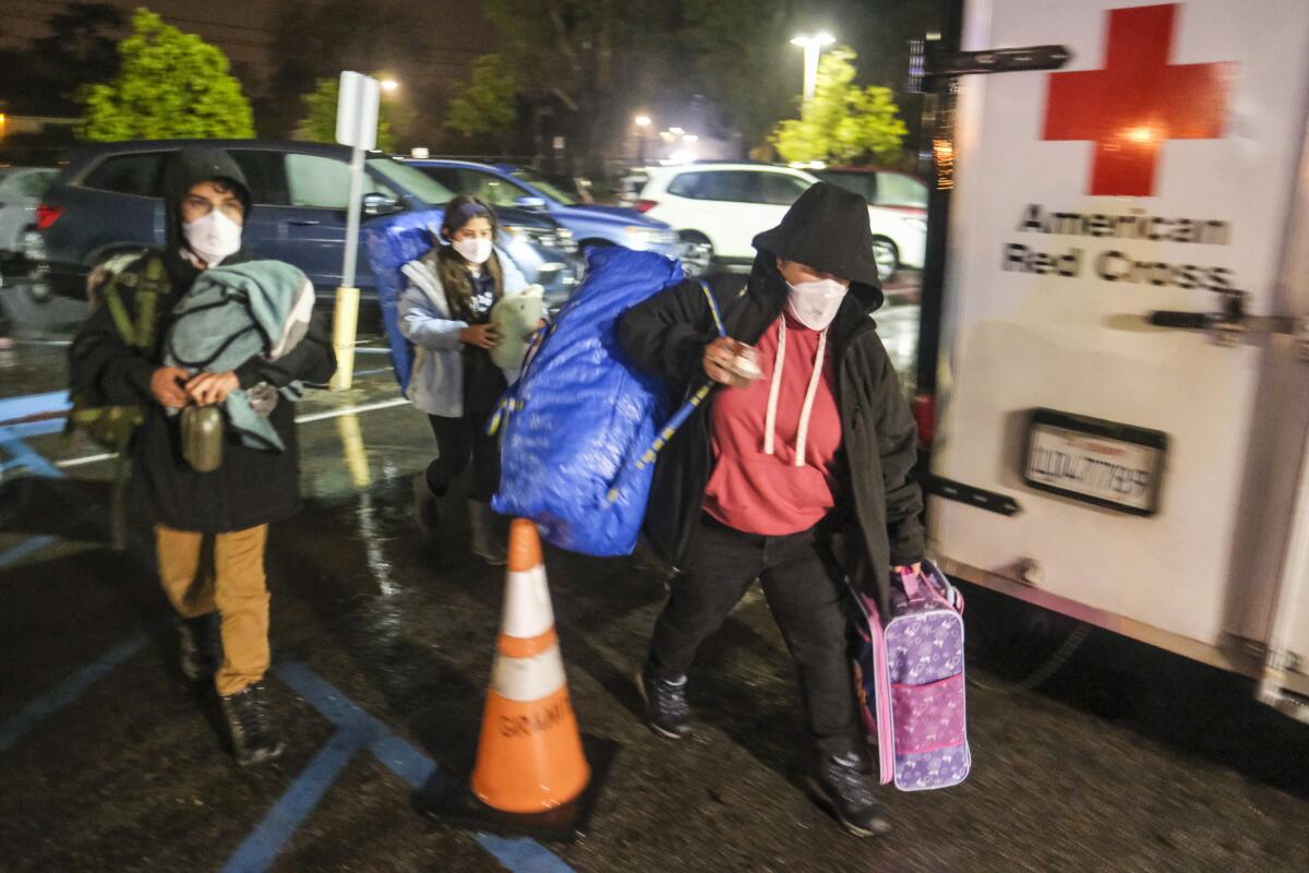 People carry bags and walk behind an American Red Cross vehicle.