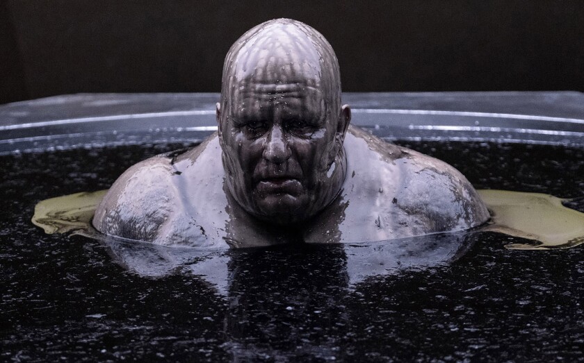 A bald and bloated Stellan Skarsgård sits in a vat of muddy-looking liquid as Baron Harkonnen in a scene from "Dune."