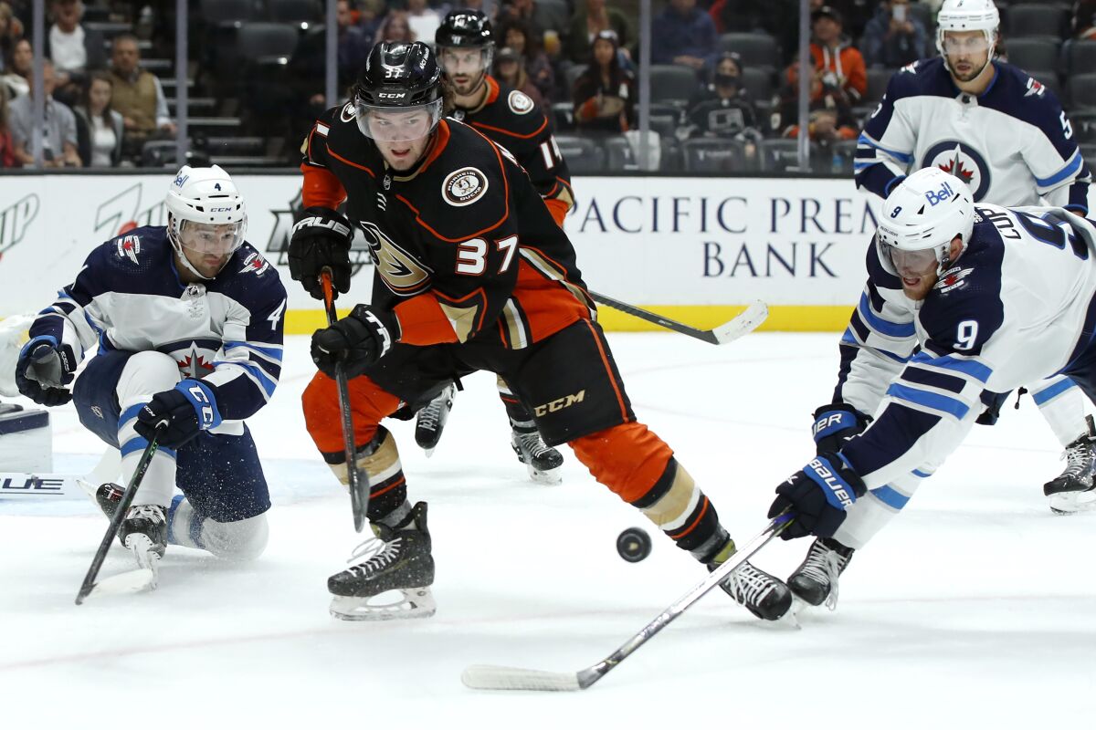 Ducks center Mason McTavish and Winnipeg Jets center Andrew Copp work for the puck with defenseman Neal Pionk watching.