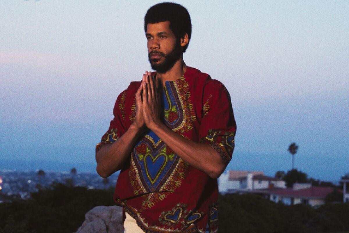 A man in a patterned maroon shirt praying outdoors