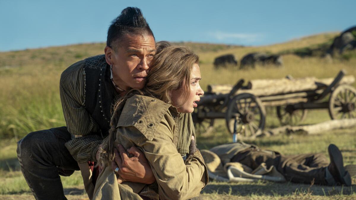 A man holds a woman protectively on a prairie as both look shocked.