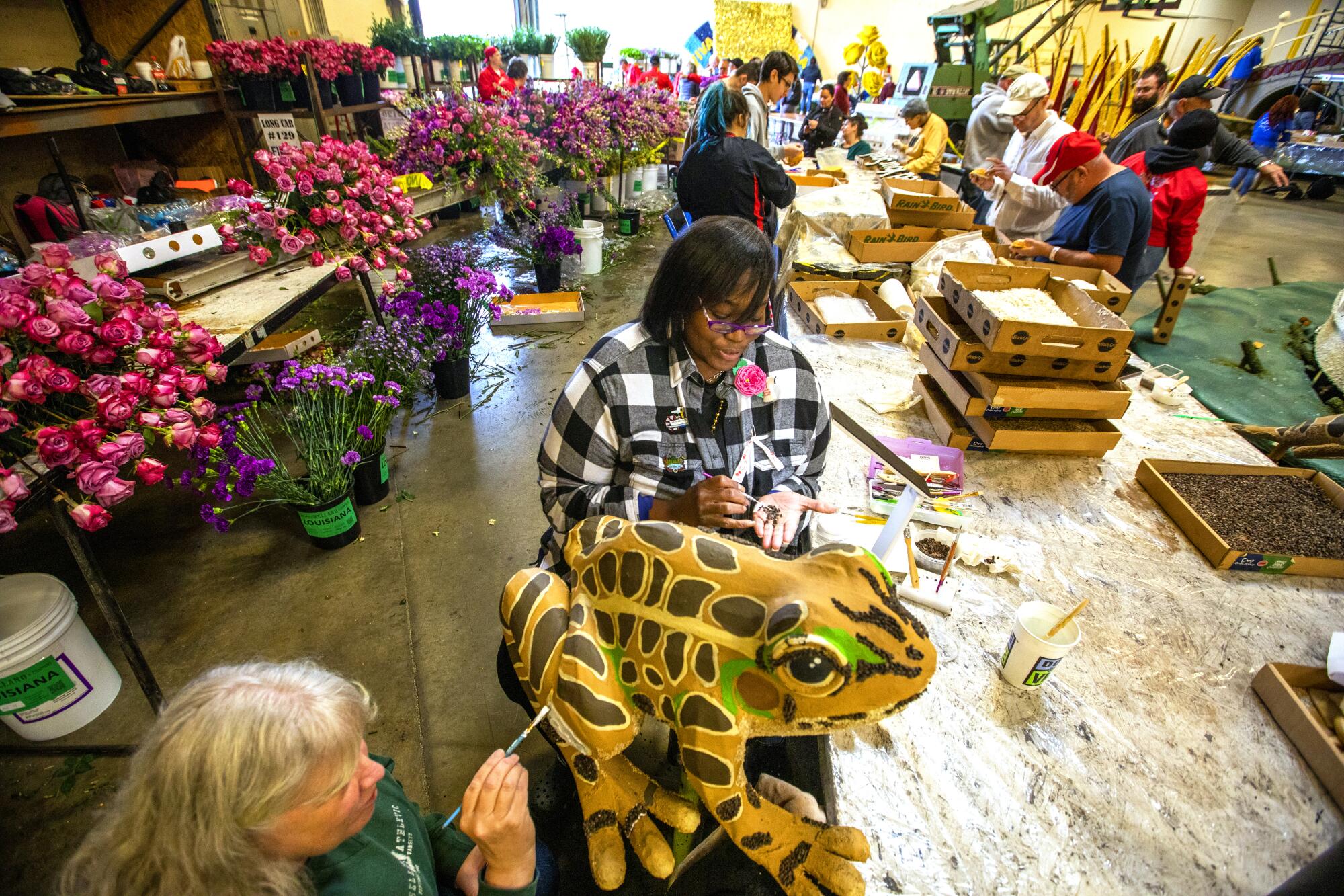 Two women work on a big brown and yellow frog for a float