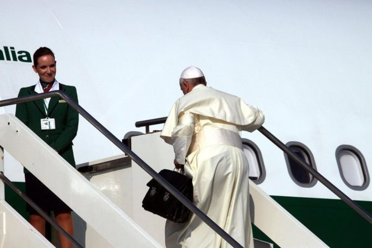 Pope Francis carries his bag up the stairs of his plane Monday as he leaves Rome for Brazil.