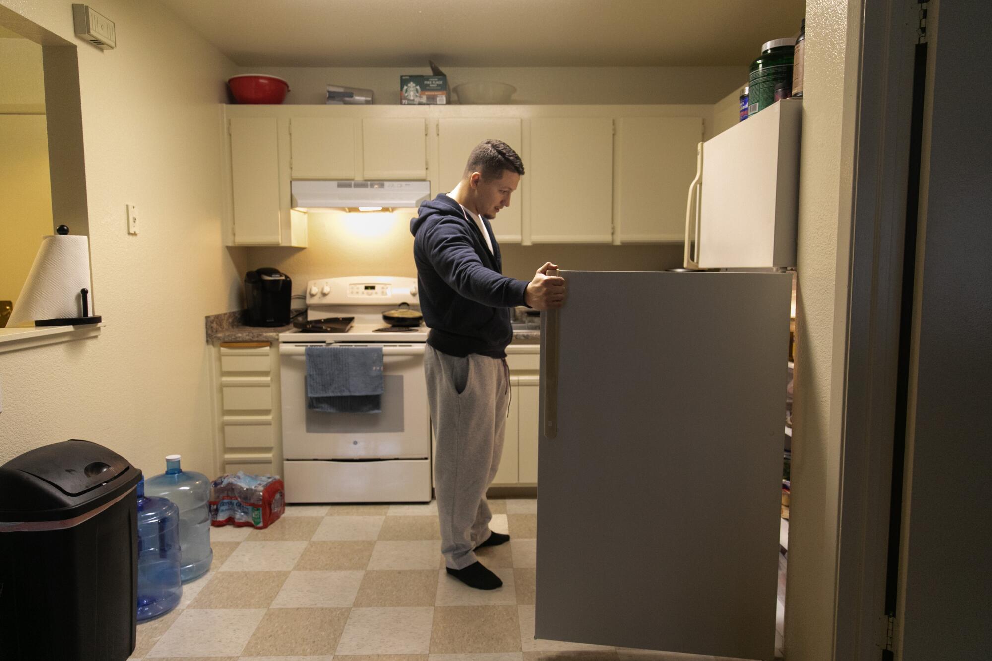 A man stands in front of an open refrigerator in a kitchen.