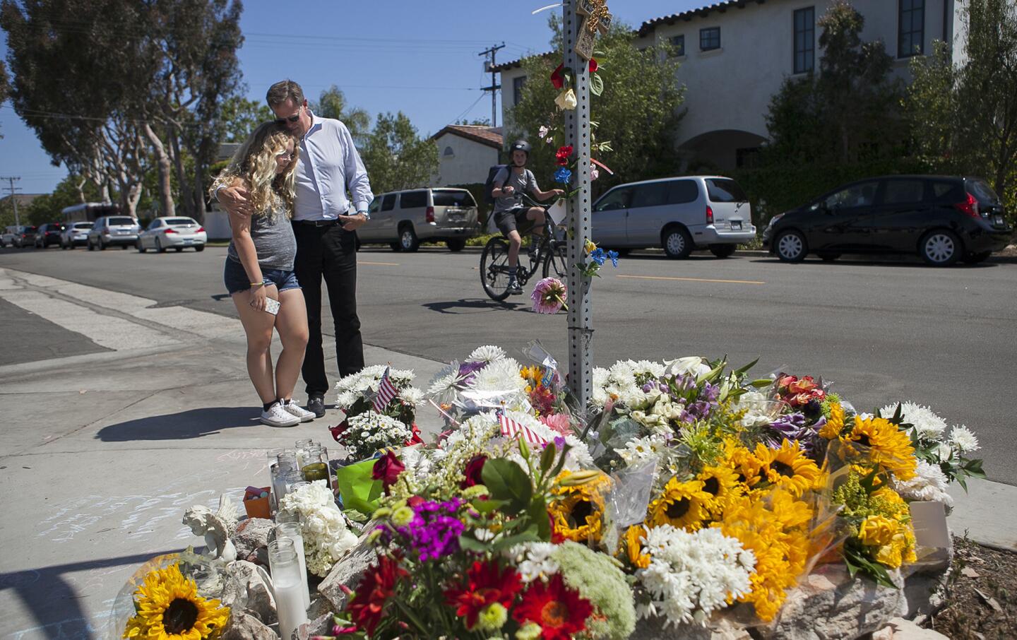 Kent Barkouras hugs his daughter Sara near a makeshift memorial for an 8-year-old boy who was struck and killed by a trash truck Wednesday at the intersection of 15th Street and Michael Place in Newport Beach.