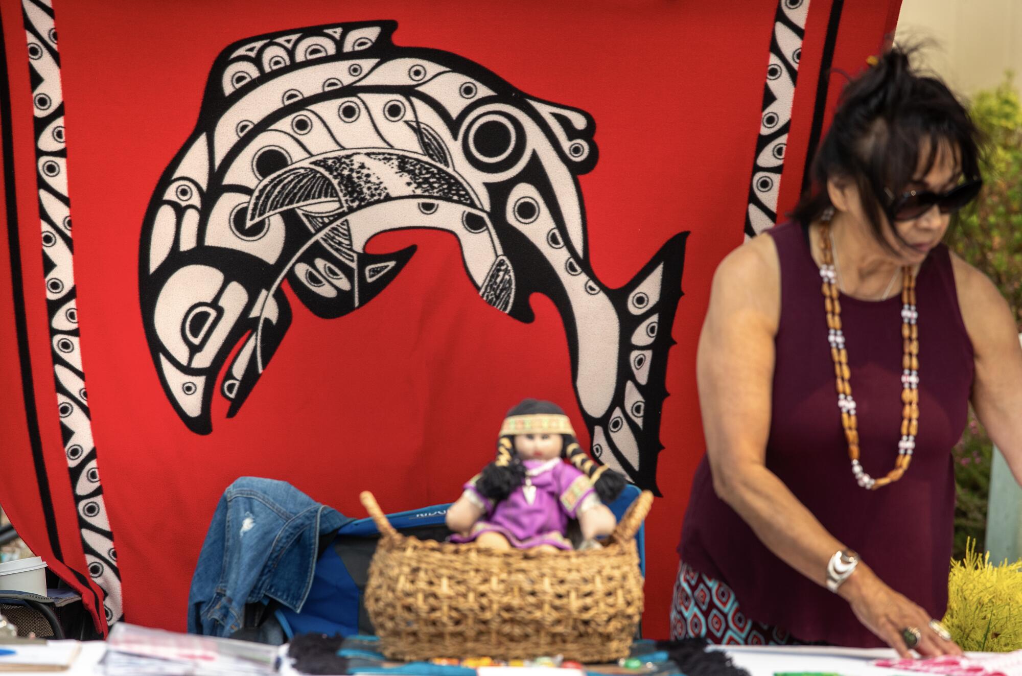 A woman stands at a festival booth beside an illustration of a salmon.