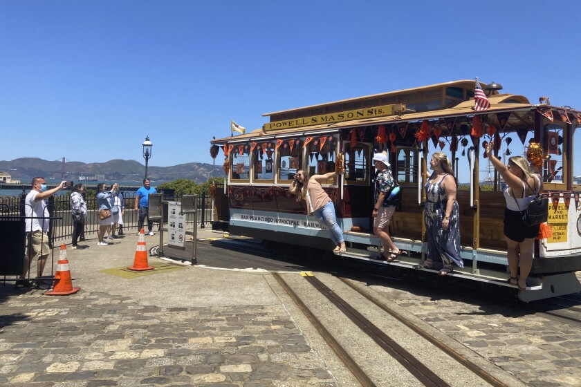 People pose for pictures on a cable car at the Hyde Street cable car turnaround in San Francisco on Tuesday, June 15, 2021. The mayor announced Tuesday that the famed cable cars would be running again in August after being halted at the start of the pandemic. (AP Photo/Olga Rodriguez)