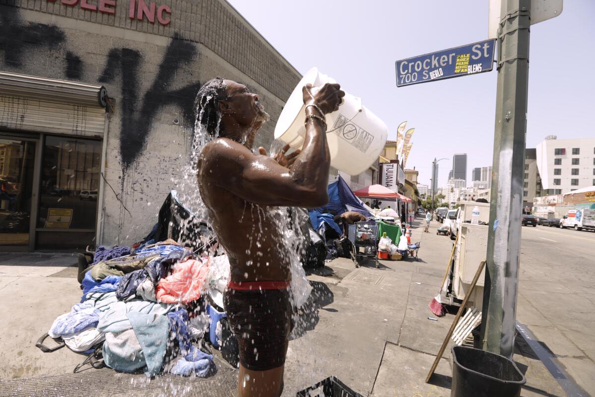 A man on a street corner washes himself by pouring a bucket of water on his chest.