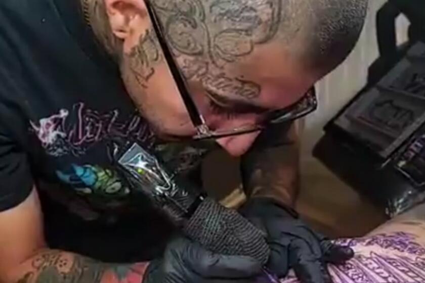 Tattoo artist Eric Reyna works on a back piece for his friend, Miguel Rodriguez, that features the graffiti covered Oceanwide Plaza.