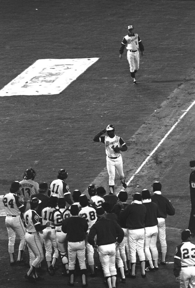 Hank Aaron tips his hat to fans and teammates greeting him at home plate