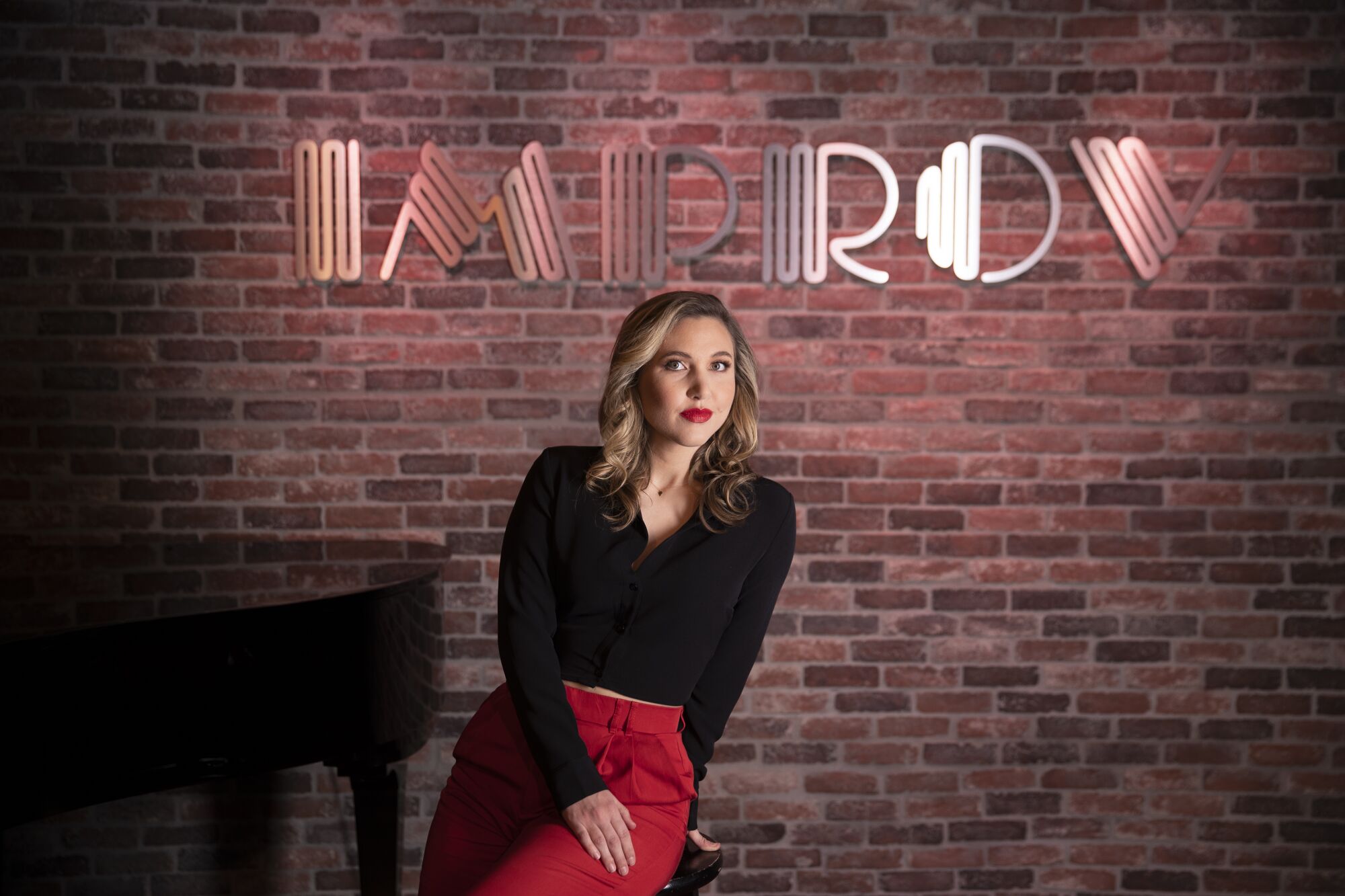 Comedian Taylor Tomlinson sits on a stool on the the Hollywood Improv stage