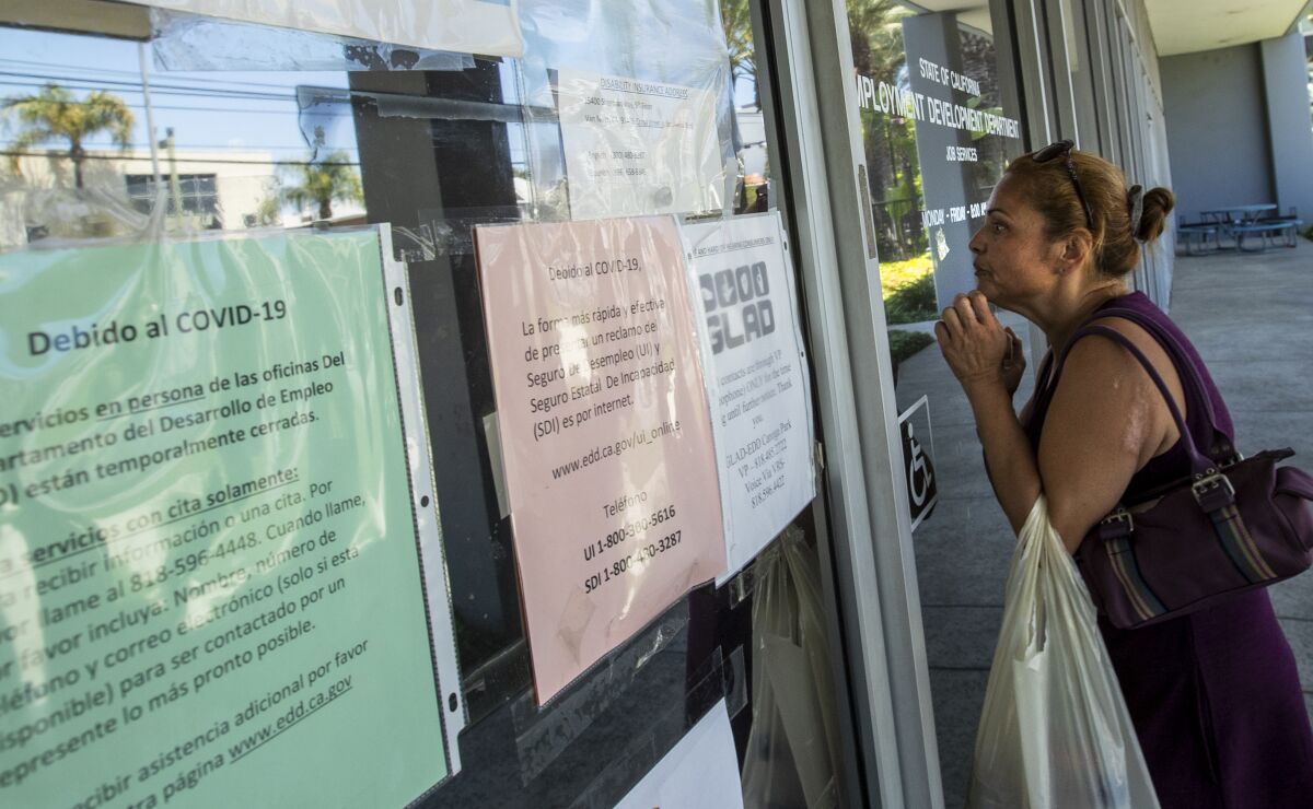A woman looks through the glass front door of the closed California Employment Development Department office in Canoga Park