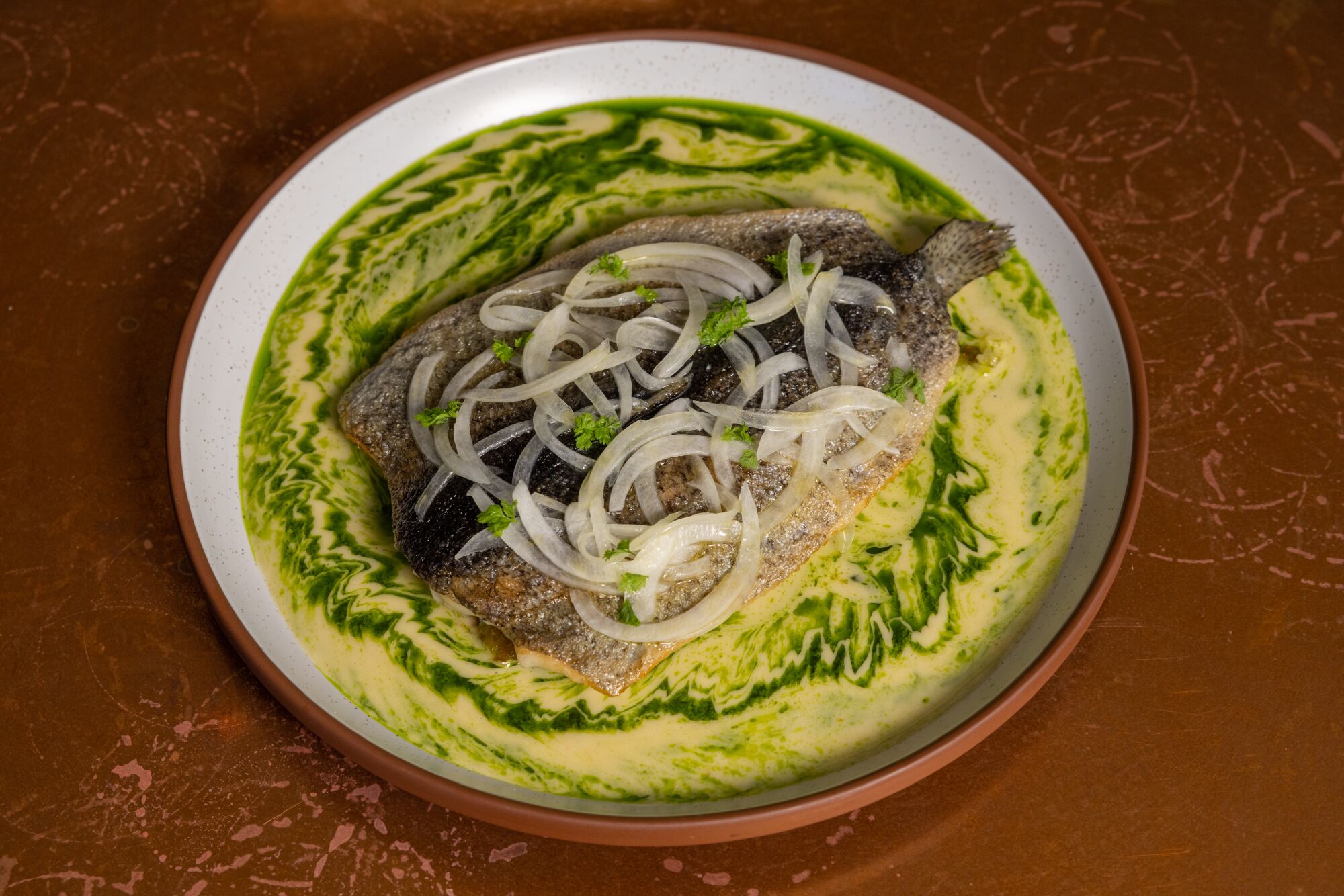 A plate of trout topped with onions and sitting in a yellow and green sauce