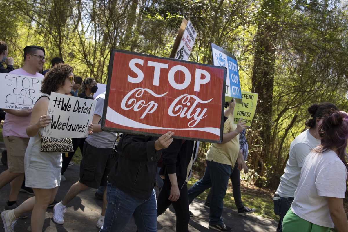 Environmental activists hold signs, one reading "Stop Coy City," and march through a forest.